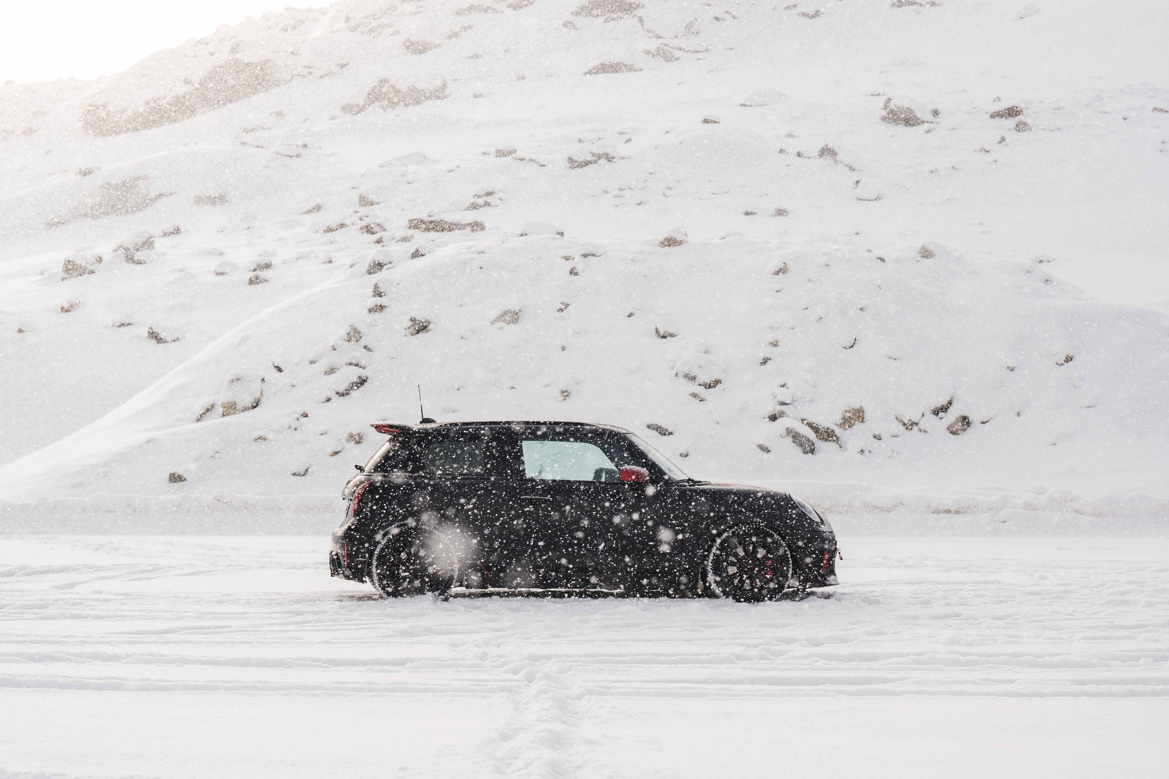 Rear view of a MINI Cooper JCW driving through the snow.